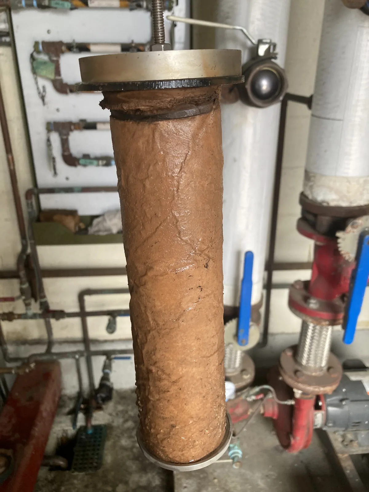 Filter sleeve pulled from its housing, completely caked in rust-colored sludge